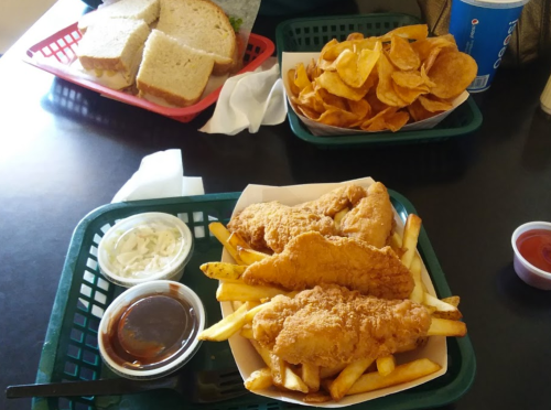 A meal featuring fried fish and fries with coleslaw and dipping sauce, alongside a basket of chips and sandwiches.