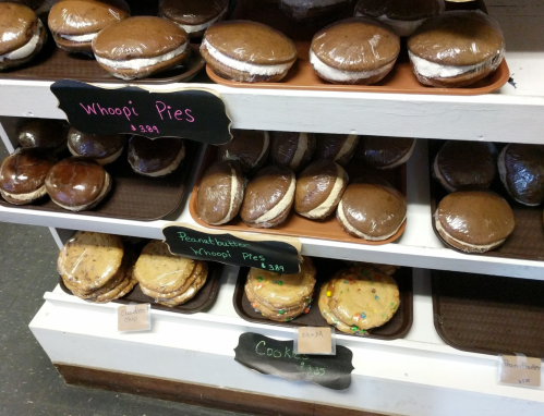Display of various whoopie pies and cookies, wrapped in plastic, with labels for flavors and prices.