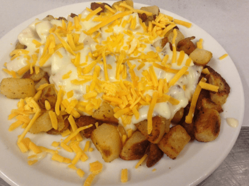A plate of crispy potato cubes topped with melted cheese and creamy sauce, garnished with shredded cheddar cheese.