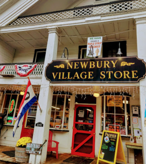 Front view of Newbury Village Store, featuring a sign, colorful flags, and festive decorations.