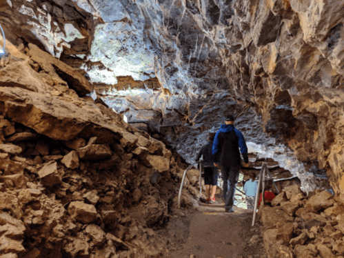 A dimly lit cave with rocky walls and a dirt path, where people are walking along a railing.