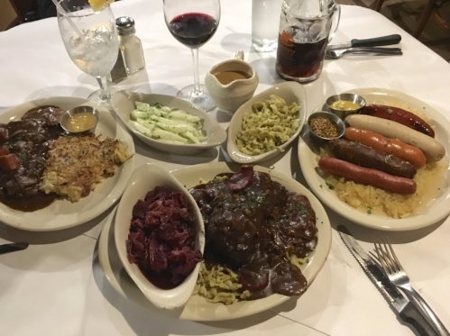 A table set with two plates of hearty German dishes, including sausages, red cabbage, sauerkraut, and sides.