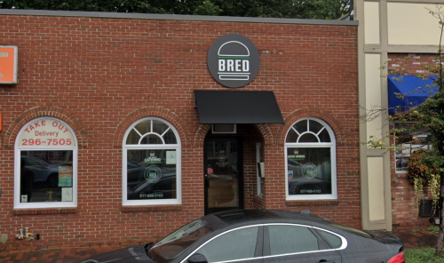 Exterior of a brick restaurant named "BRED" with large windows and a black awning, parked car in front.
