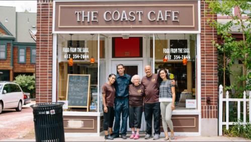 A group of five people stands outside The Coast Cafe, smiling in front of the restaurant's welcoming entrance.