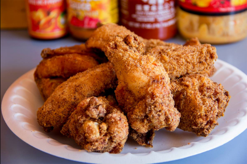 A plate of crispy, golden-brown fried chicken wings, surrounded by various sauces in the background.