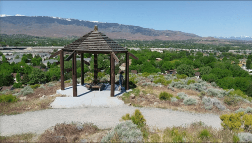 A gazebo on a hilltop overlooking a green valley and distant mountains under a clear blue sky.