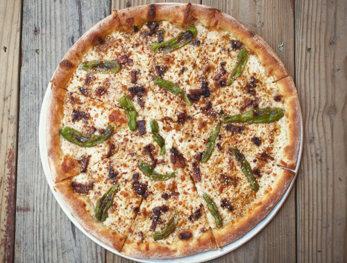 A freshly baked pizza topped with cheese, green peppers, and crispy bacon on a wooden table.