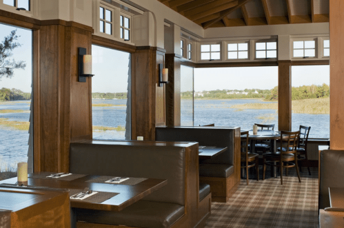 Cozy restaurant interior with wooden accents, large windows overlooking a scenic water view and comfortable seating.