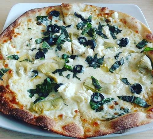 A freshly baked pizza topped with cheese, artichokes, black olives, and fresh basil on a golden crust.