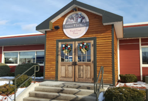 A wooden building with a sign reading "Vermont Tap House" and festive wreaths on the doors, surrounded by snow.