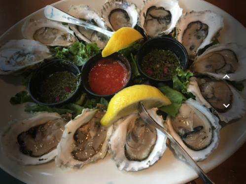 A platter of fresh oysters on a bed of lettuce, served with lemon wedges and dipping sauces.