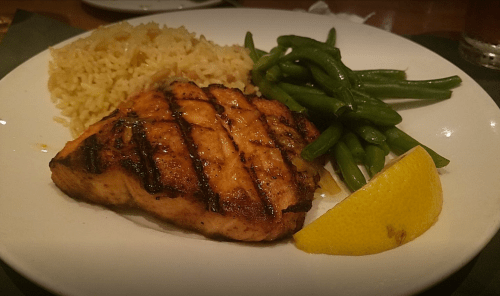 Grilled salmon fillet with rice, green beans, and a lemon wedge on a white plate.