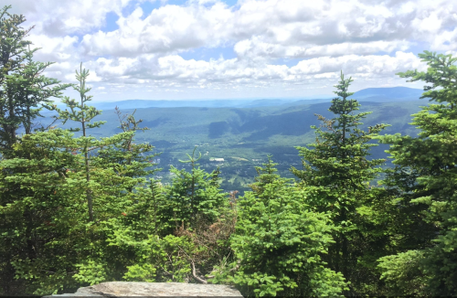 A panoramic view of lush green mountains and valleys under a partly cloudy sky.