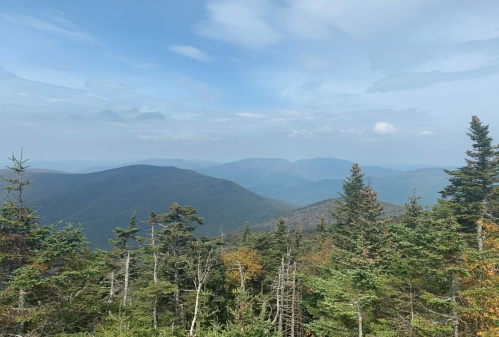 A panoramic view of rolling mountains and trees under a blue sky with scattered clouds.
