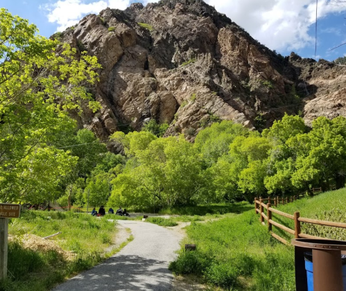 A winding path leads through lush greenery, with a rocky mountain backdrop and people sitting in the distance.