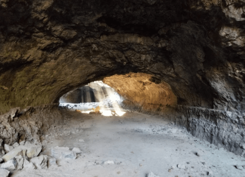 A dimly lit cave with a rocky interior, featuring a light source illuminating the entrance.