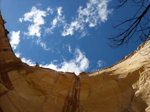 View looking up at a blue sky with clouds, framed by the rocky walls of a canyon.