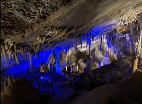 A stunning cave interior with illuminated stalactites and stalagmites, showcasing blue lighting and intricate rock formations.