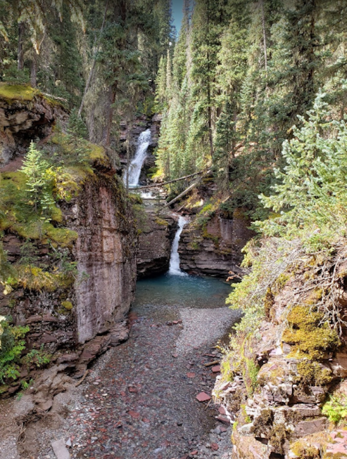 A serene landscape featuring a waterfall cascading through rocky cliffs, surrounded by lush green trees.