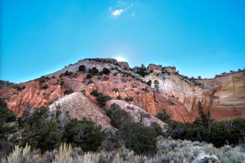 A colorful rocky hillside under a clear blue sky, with sparse vegetation in the foreground.