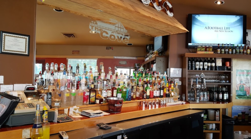 A bar with a wide selection of liquor bottles, a cash register, and a TV displaying a sports program.