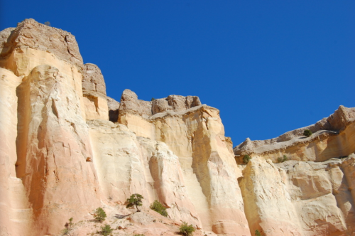 Colorful rock formations under a clear blue sky, showcasing layers of beige, pink, and orange hues.