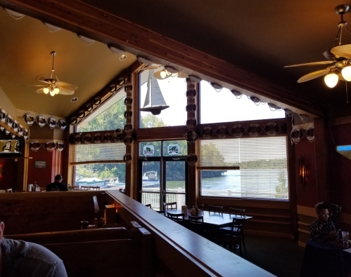 Interior of a restaurant with wooden decor, large windows overlooking a lake, and tables set for dining.