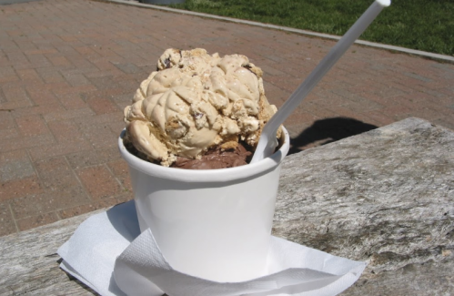 A cup of ice cream with two scoops: one chocolate and one cookie dough, resting on a wooden surface.