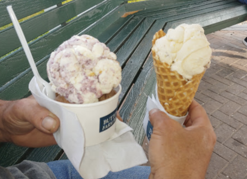 Two hands holding ice cream cones: one with purple and white swirled ice cream, the other with plain vanilla.