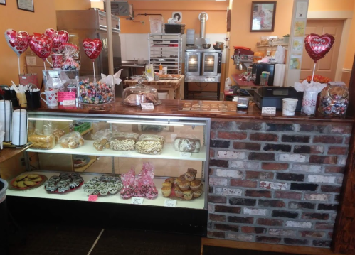 A cozy bakery display with various pastries, candies, and heart-shaped balloons, featuring a warm, inviting atmosphere.