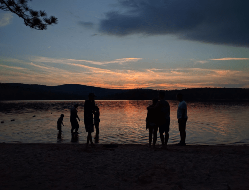 Silhouettes of people by a lake at sunset, with colorful skies and calm water reflecting the light.
