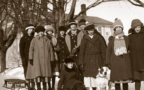 A group of women in winter clothing, smiling together in a snowy outdoor setting, with a dog in front.