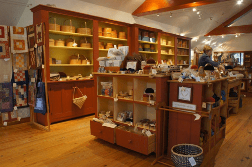 A cozy craft shop interior with wooden shelves displaying baskets, quilts, and handmade items.