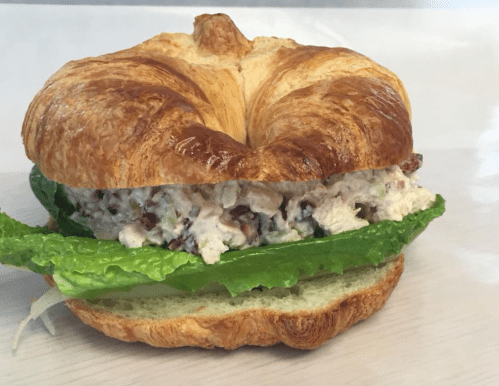 A croissant sandwich filled with chicken salad and lettuce on a light background.