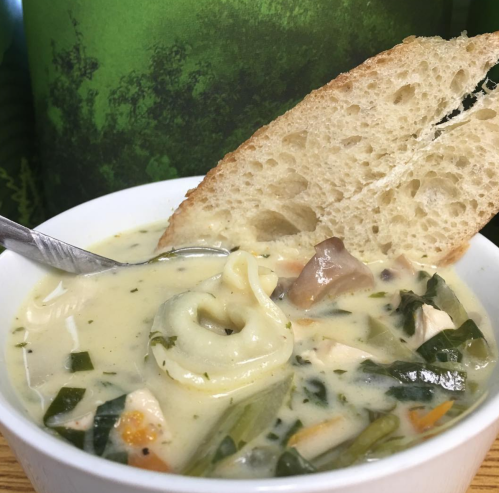 A bowl of creamy soup with vegetables and dumplings, accompanied by a slice of rustic bread.