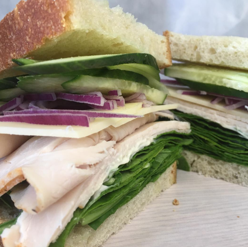 Close-up of a sandwich with layers of turkey, spinach, cucumber, and red onion between two slices of bread.