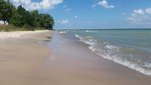 A serene beach scene with gentle waves lapping at the sandy shore under a blue sky with fluffy clouds.