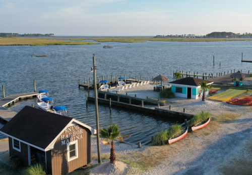 A marina with boats docked, a sandy area, and a small building labeled "Snug Harbor Marina" by the water.
