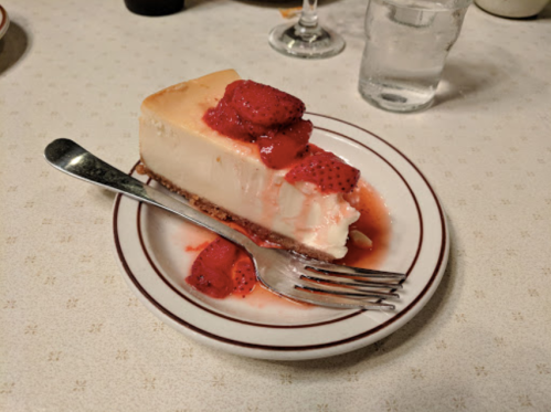 A slice of cheesecake topped with strawberries and sauce on a plate, with a fork beside it.