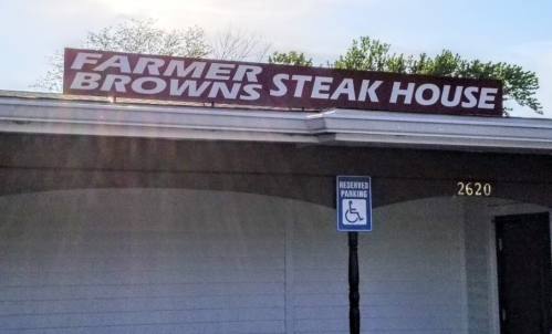 Sign for Farmer Brown's Steak House, with reserved parking sign visible in front of the building.