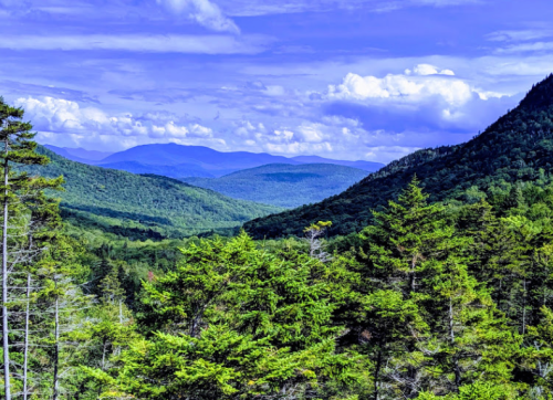 A scenic view of lush green mountains under a blue sky with fluffy clouds, showcasing a peaceful natural landscape.