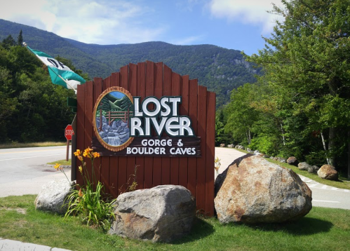 Sign for Lost River Gorge and Boulder Caves, surrounded by greenery and mountains in the background.