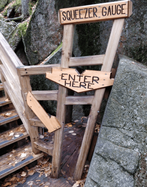 Wooden structure labeled "Squeezer Gauge" with an arrow pointing to "Enter Here," set against a rocky background.