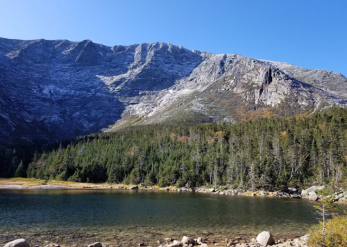 A serene mountain landscape with a clear lake in the foreground and snow-capped peaks in the background.