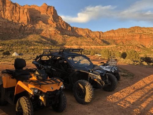 Three ATVs parked in a scenic desert landscape with red rock formations and a sign for Zion ATV rentals.