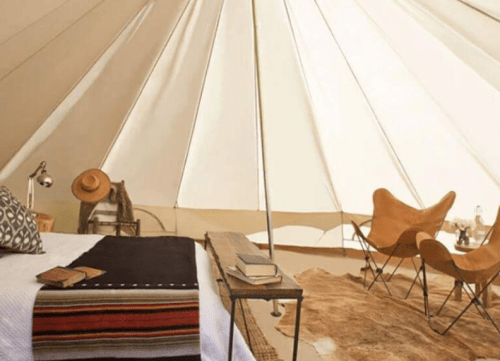 Cozy glamping tent interior with a bed, chairs, and decorative elements, featuring natural light and earthy tones.