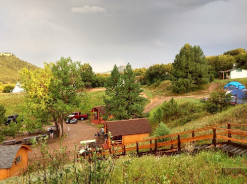 A scenic view of a campsite with cabins, tents, and trees under a cloudy sky.