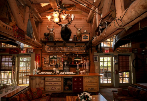 Cozy rustic interior of a lodge with wooden beams, a bar, and mounted animal heads on the walls.