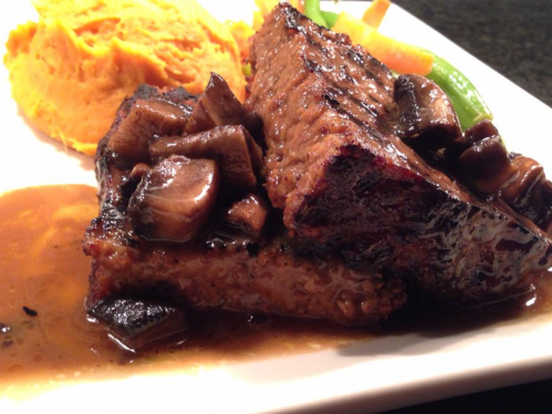 A plate featuring tender beef brisket topped with mushrooms, served with sweet potato mash and green beans.