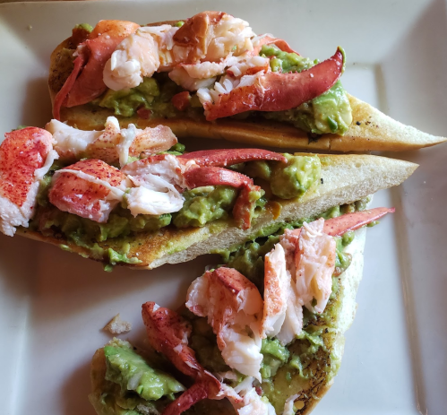 Two toasted bread halves topped with guacamole and pieces of lobster meat.